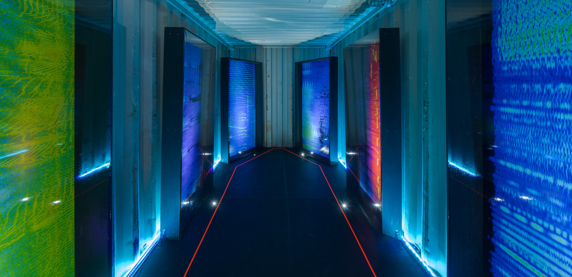 Eco-location, install view inside shipping container, spectrogram panels lit blue and green, red LED lines on floor.