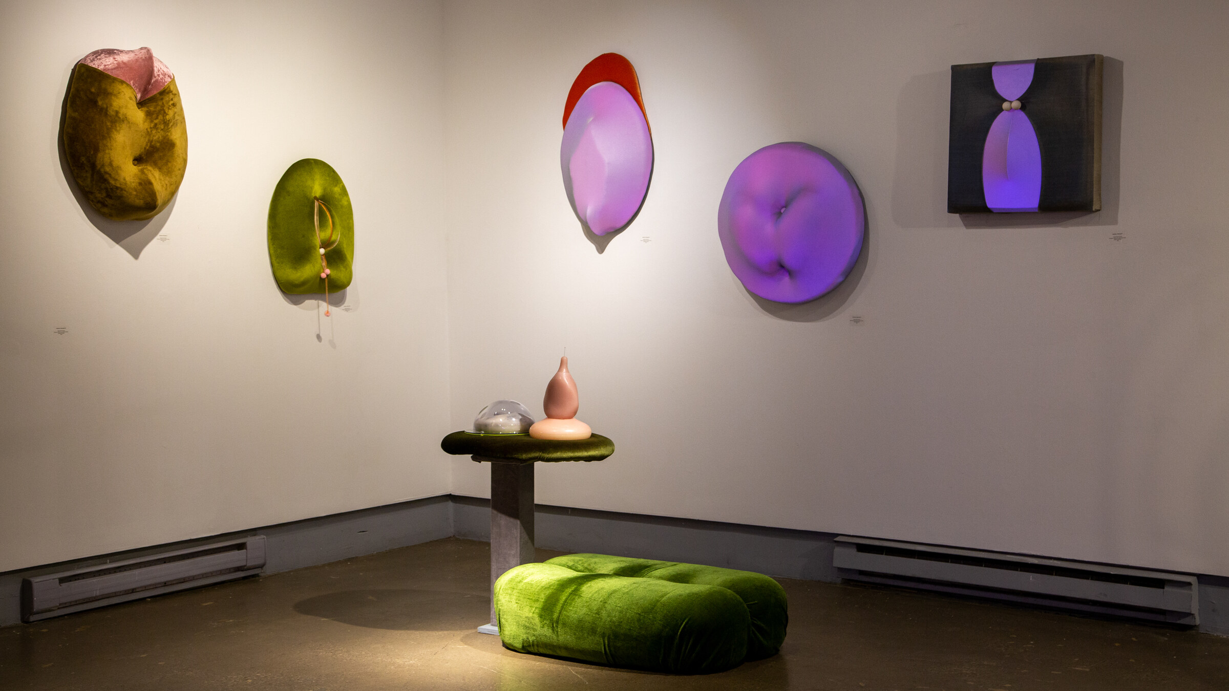 Polymère, Polymorphe — install view, gallery corner with mustard and olive velour wall sculptures, wax forms on green velvet pedestal.